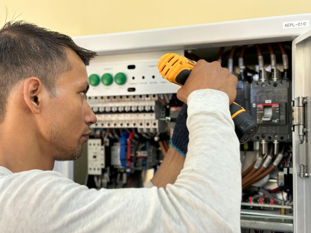 electrician reviewing electrical panel with certification documents and wiring schematics