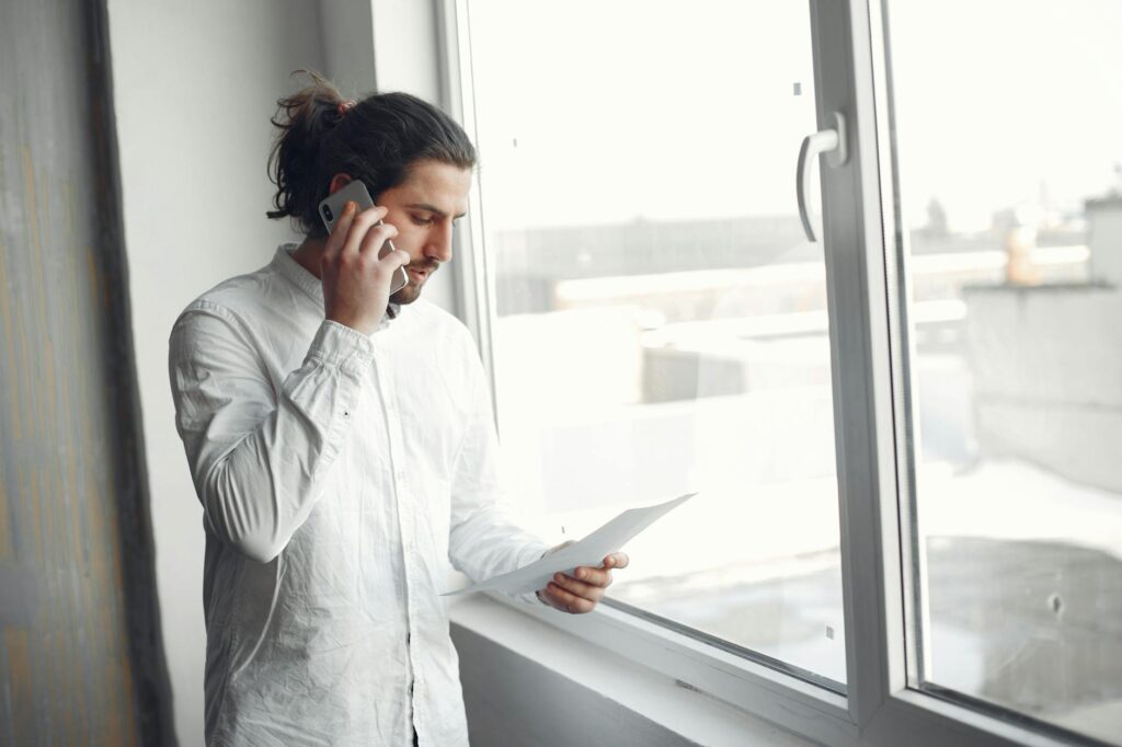 frustrated homeowner checking phone while holding NIDI SLO documents beside electrical panel